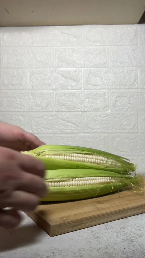 White man places fresh raw white cob of corn on wooden cutting board Stock Footage 281126832