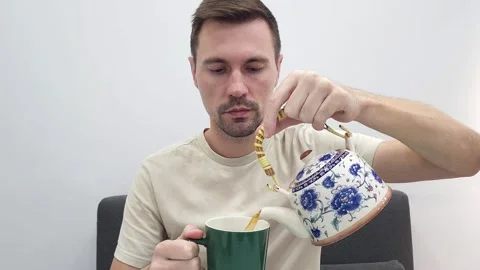 White man pouring tea from a decorative teapot into a green cup Stock Footage 282610744