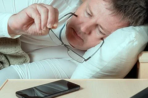 White man puts eyeglasses on while lying in bed Stock Photos