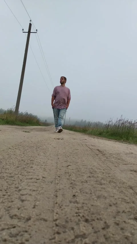 White man in red and white striped sweater walks along village road Stock Footage 277562263