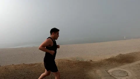 A white man running uphill on the beach in a black sleeveless shirt with the bac Stock-Footage 194444779