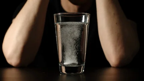 White man sits at the table, takes white pill and throws it into glass of water Vídeo Stock 104022897