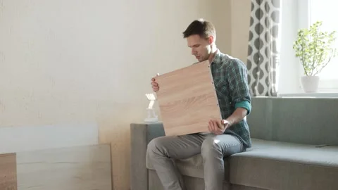 White man is sitting, picking up piece of furniture, examining it. Stock Footage 220687939