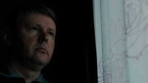 White man thoughtfully looks out the window of the room in the evening Stock Footage 127948377