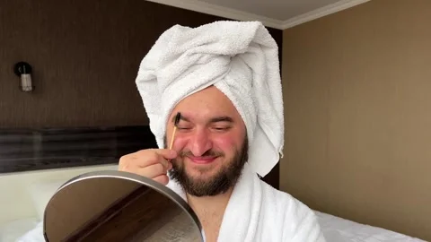 White man in towel on head combs eyebrows in hotel room Video stock 276739847
