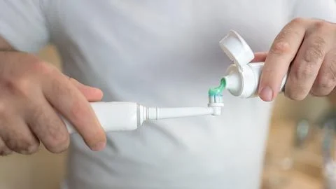 White man's hands pouring thootpaste into an electric toothbrush. Stock Photos