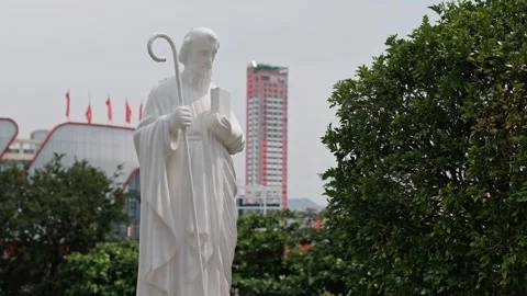 White marble statue of a saint holding a staff and book with city buildings 스톡 동영상 340207100