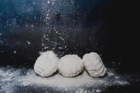 White marshmallows on a black background with crumbling powdered sugar Stock Photos