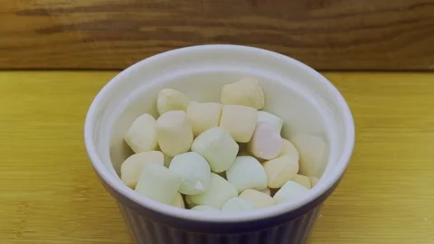 White Marshmallows Falling into Ceramic Bowl on Wooden Table Stock Footage 343723824