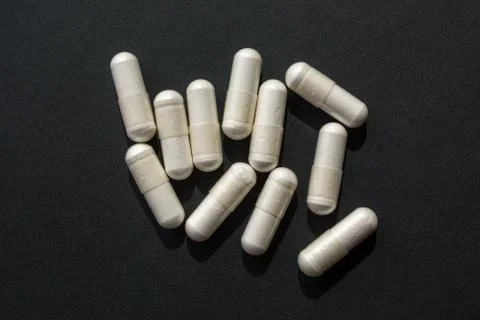 White medical capsules close-up on a black background Stock Photos