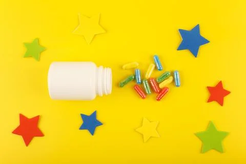 White medication bottle with oval multicolored pills spilled against yellow Stock Photos
