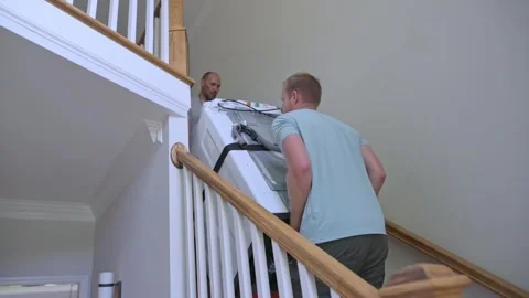 White men movers carrying washer down stairwell, coordinated lift around Stock Footage 323092171