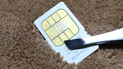 A white mini-SIM card with a golden chip is held with tweezers against a backgro Stock Footage 149221153