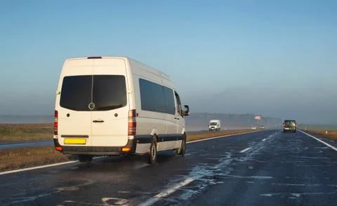 A white minibus transports people to another city on a wet highway. The concept Stock Photos