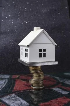 White model house on top of a stack of coins, on dark background Stock Photos