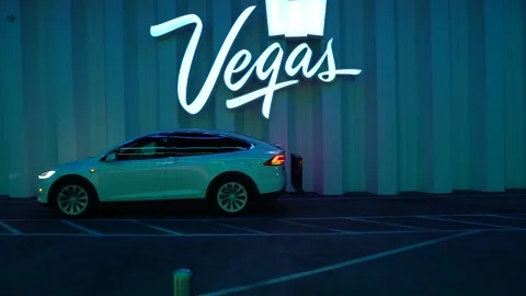 White Model Y Tesla drives passed Neon Vegas Sign at the LVCC Loop in Las Vegas Stock Footage 225537180