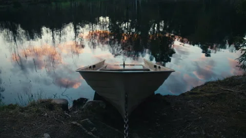 White Moored Rowboat Chained at the Shore of a Calm Lake With Dusk Reflections Stock Footage 338115035