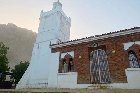 White mosque tower with brick facade and mountain backdrop at sunrise Stock Photos