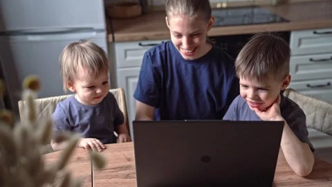 White mother and sons smiling at laptop together in kitchen, shared laughter, Stock Footage 336974322