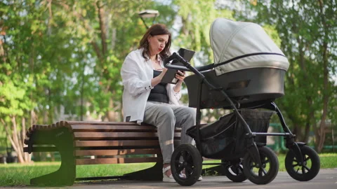 White mother on bench with stroller reviewing decree on tablet, relaxed Video stock 346402463