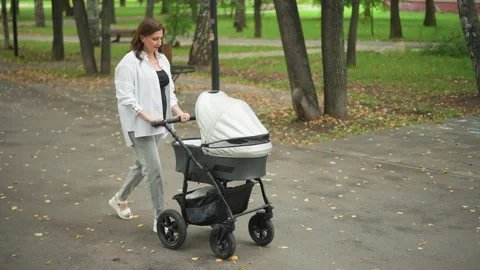 White mother checking stroller and comforting baby at park, gentle interaction Video stock 346409458