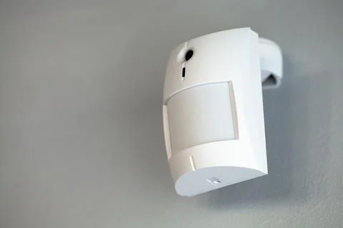 A white motion sensor camera on a gray wall, providing security and surveillance Stock Photos