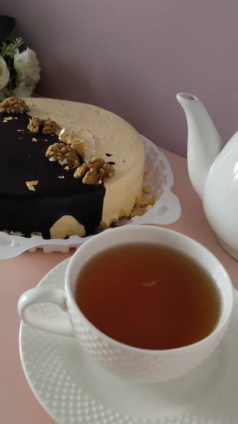 A white mug of black tea on a pink table, a cake with cream and chocolate in the Stock Footage 324782437