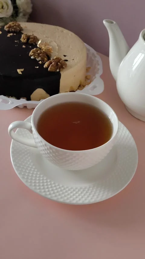 A white mug of black tea on a pink table, a cake with cream and chocolate in the Stock Footage 324782467