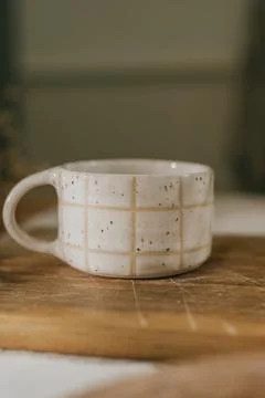 A white mug with a checkered pattern sits on a wooden cutting board Stock Photos