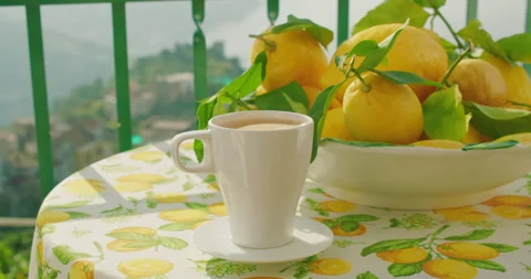 White mug of coffee on a patterned tablecloth with lemons, outdoors. The table Stock Footage 274759931