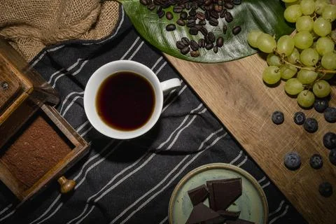 A white mug with dark coffee, surrounded by roasted beans and fruit on a wo.. Photos