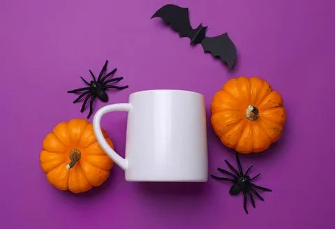White mug with pumpkins and plastic spiders on purple background Stock Photos