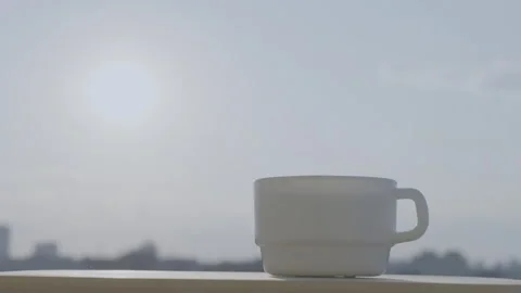 White mug rests on a ledge, overlooking a city under a hazy sky Stock Footage 295420209