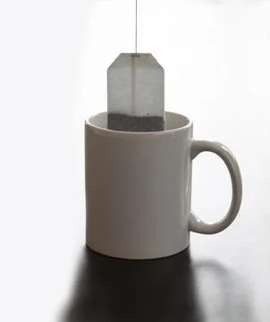 White mug stands on a table with tea bag hanging  by a string. Backlit image Stock Photos