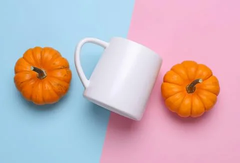 White mug with two small orange pumpkins on pastel blue and pink background Stock Photos