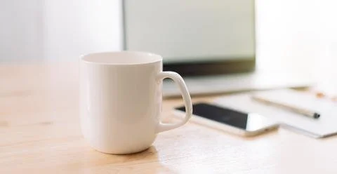 White mug without inscriptions opposite laptop and notepad with pen on wood.. Stock Photos