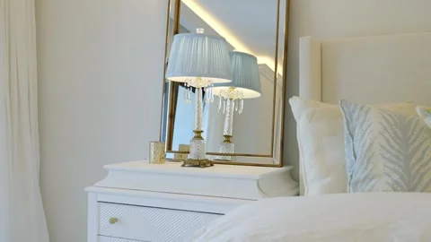 White night stand table with mirror and shining lamp placed near soft bed Stock Footage 242943710