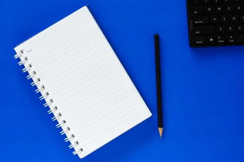 White note book and black pencil and black keyboard on blue color background  Stock Photos