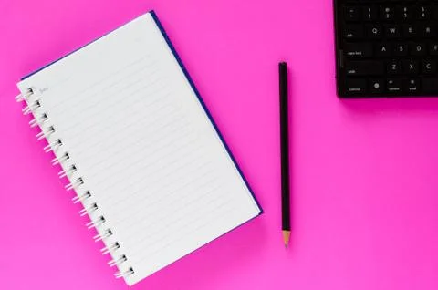 White note book and black pencil and black keyboard on pink color background  Stock Photos