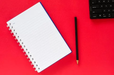 White note book and black pencil and black keyboard on red color background w Stock Photos