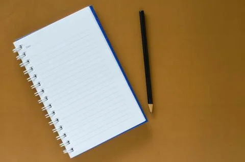 White note book and black pencil on brown color background with copy space. Stock Photos