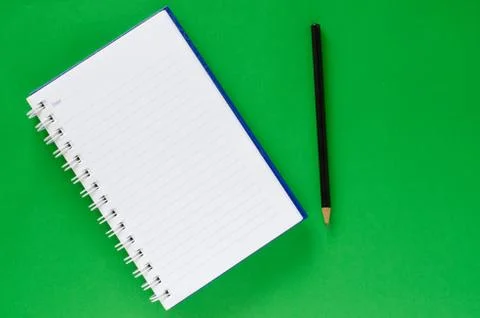 White note book and black pencil on green color background with copy space. Stock Photos