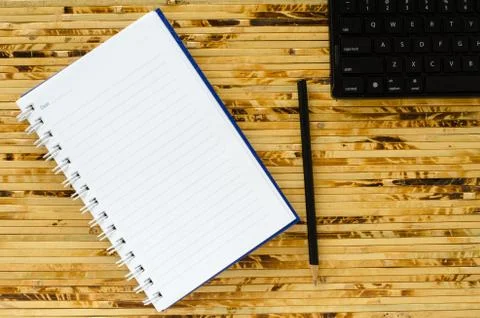 White note book and black pencil and black keyboard on bamboo color backgroun Stock Photos