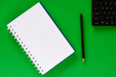 White note book and black pencil and black keyboard on green color background Stock Photos