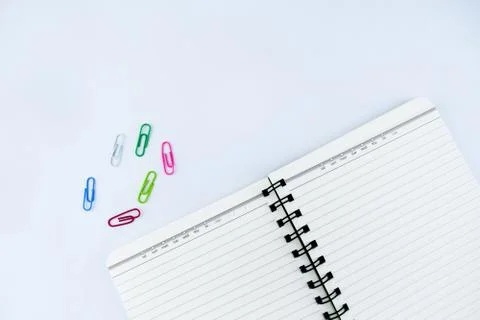 A white notebook along side some different colored paper clips on an isolated Stock Photos