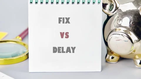 A white notebook displaying the words fix versus delay is placed on a grey Stock Footage 335095021