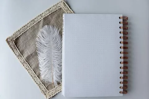 White notebook placed on a cloth with a feather beside it on a clean surface in 스톡 사진