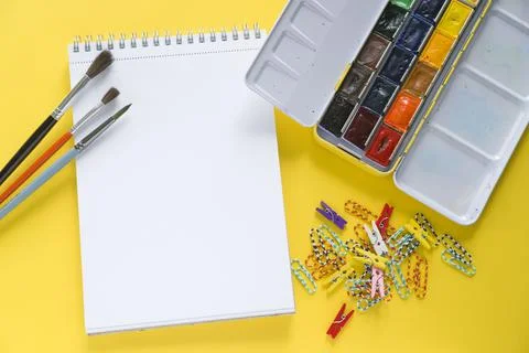 White notepad for drawing on a yellow background. Watercolor paints and brush Stock Photos