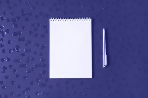 White notepad with silver pen on background with heart shaped confetti. Ton.. Fotos de archivo