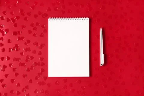 White notepad with silver pen on red background with heart shaped confetti Stock Photos
